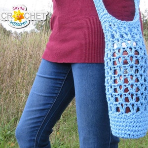 May include: A light blue crocheted tote bag with a star-shaped pattern. The bag is being worn by a person wearing blue jeans and a maroon sweater.