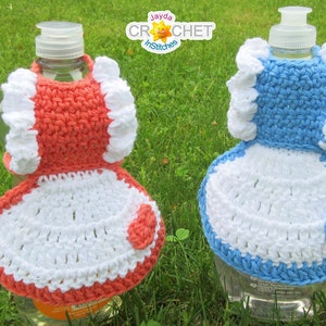 May include: Two crocheted bottle covers in the shape of dresses. One is coral with white trim and the other is light blue with white trim. Both have white crocheted skirts and a white heart on the front.