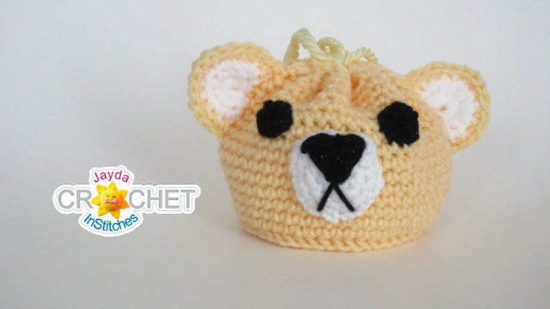May include: A crocheted yellow bear-shaped drawstring bag with black eyes and a black nose. The bag has a white crocheted nose and white crocheted ears.