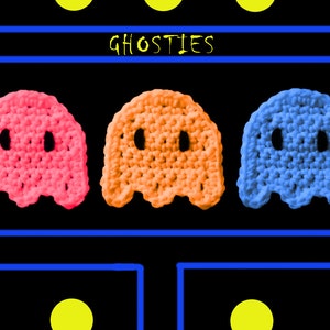 May include: Three crocheted ghost figures in pink, orange, and blue, arranged in a row with the word "GHOSTIES" above them.