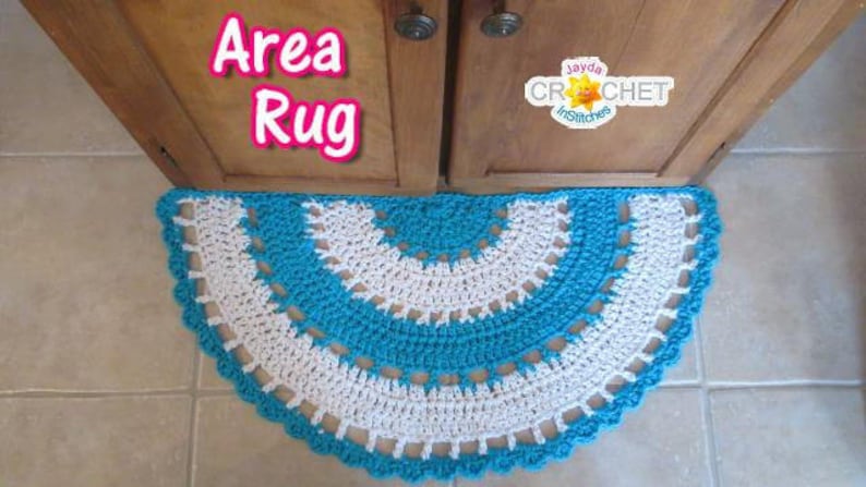 May include: A crocheted area rug in a half-circle shape with a white and turquoise design. The rug is placed in front of a wooden cabinet door.