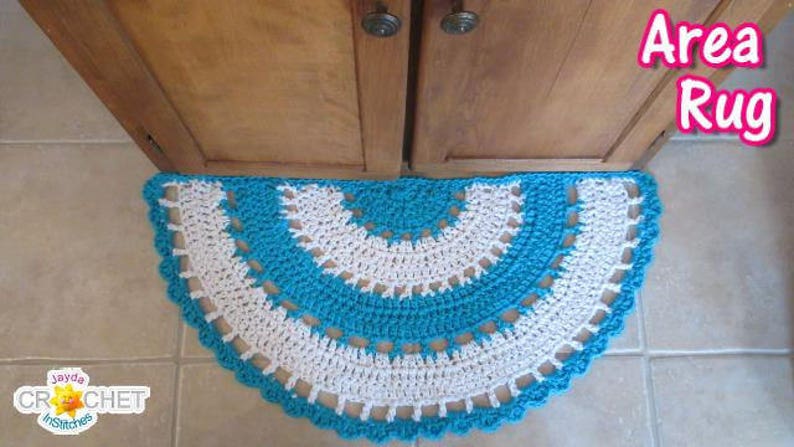 May include: A crocheted area rug in a half-circle shape with a white and turquoise design. The rug is placed in front of a wooden cabinet door.