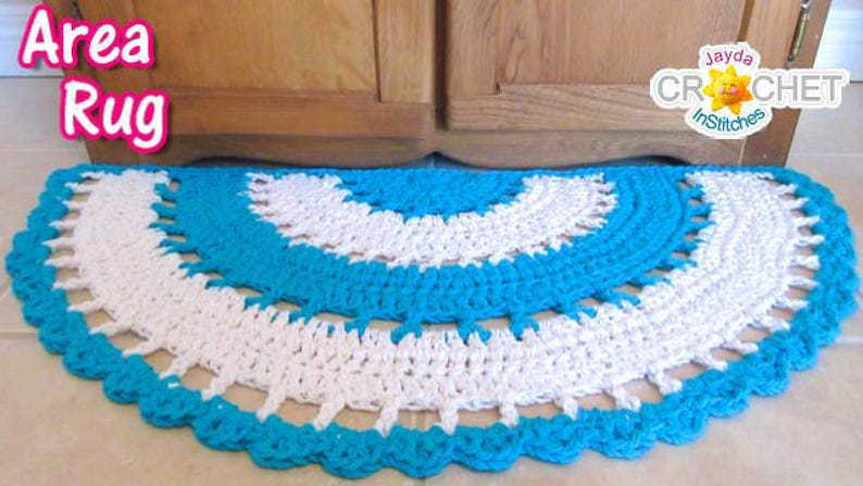 May include: A crocheted area rug in a half-circle shape with a white and turquoise colour pattern. The rug is made with a simple stitch and has a scalloped edge. The text "Area Rug" is visible in the top left corner of the image.