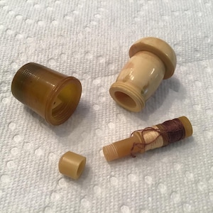 May include: A set of four vintage sewing tools, including a spool holder, a thimble, a needle threader, and a spool of thread. The tools are made of a light brown plastic and have a worn, antique look.