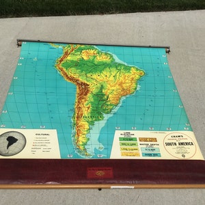 May include: A vintage, rolled-up map of South America with a green and brown topographical relief design. The map is labeled "Cram's Physical Political Map No. 2 South America" and includes a key for land elevation and water depth.