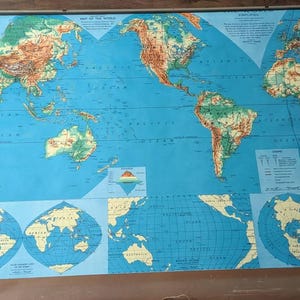 May include: A vintage world map on a roller, featuring continents in shades of brown and green against a blue ocean background. The map includes detailed geographical features and is labeled with the title "MAP OF THE WORLD".