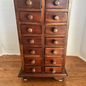 May include: A wooden cabinet with 12 drawers. The cabinet is dark brown and has a simple design.