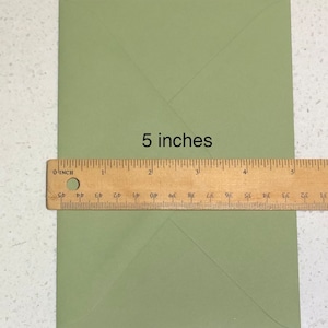 May include: A green envelope measuring 5 inches in length. The envelope is folded in half and has a crease down the center.