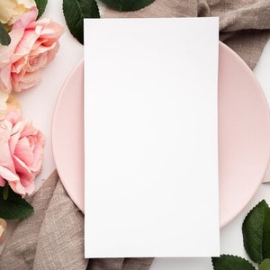 May include: A blank white card on a pink plate with a brown linen napkin and pink roses around it.