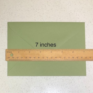 May include: A green envelope measuring 7 inches in length. A ruler is placed below the envelope to show the measurement.