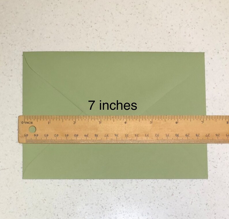 May include: A green envelope measuring 7 inches in length. A ruler is placed below the envelope to show the measurement.