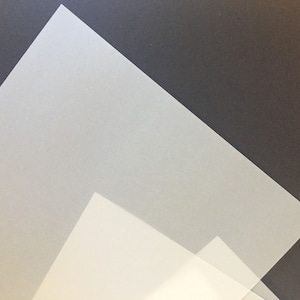 May include: Two sheets of translucent white paper, one on top of the other, with the top sheet slightly angled.
