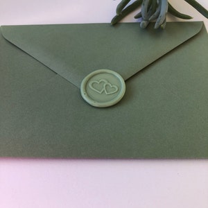 May include: A sage green envelope with a wax seal featuring two interlocking hearts.