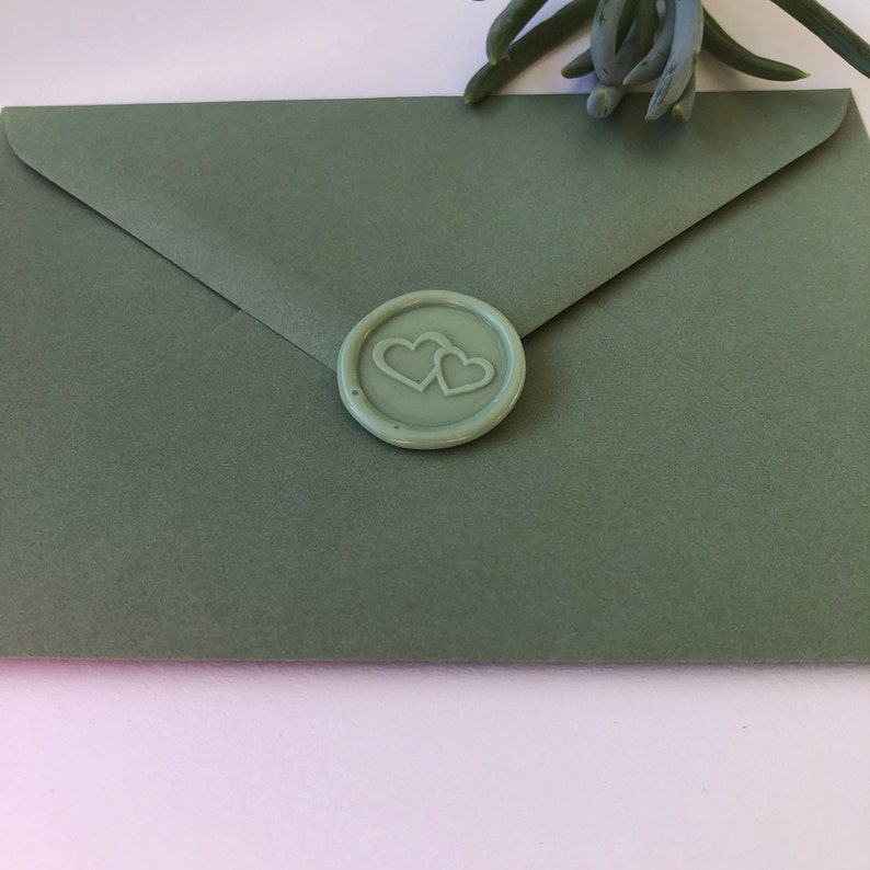 May include: A sage green envelope with a wax seal featuring two interlocking hearts.