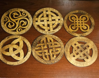 May include: Six wooden coasters with intricate Celtic knot designs. The coasters are circular and have a light brown color.
