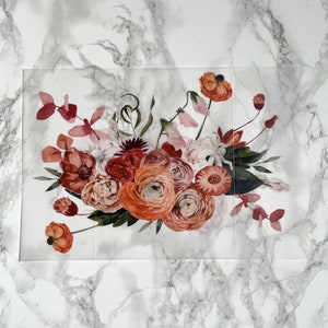 May include: A bouquet of pink, red, and orange flowers with green leaves on a white marble background.