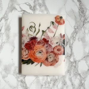 May include: A white card with a floral design featuring pink, red, and orange flowers. The flowers are arranged in a bouquet with green leaves and stems.