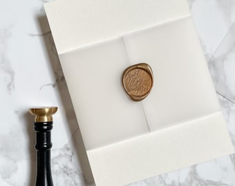 May include: A white envelope with a clear vellum overlay. A gold wax seal with the text "Best Day Ever" is on the vellum. A black and gold wax seal stamp is next to the envelope.