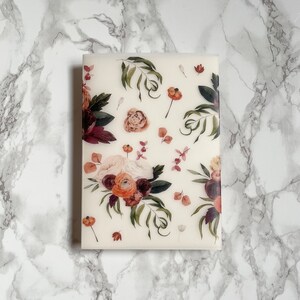 May include: A white sheet of paper with a floral design printed on it. The design features a variety of flowers in shades of pink, red, and orange, with green leaves and stems. The flowers are arranged in a loose, flowing pattern.