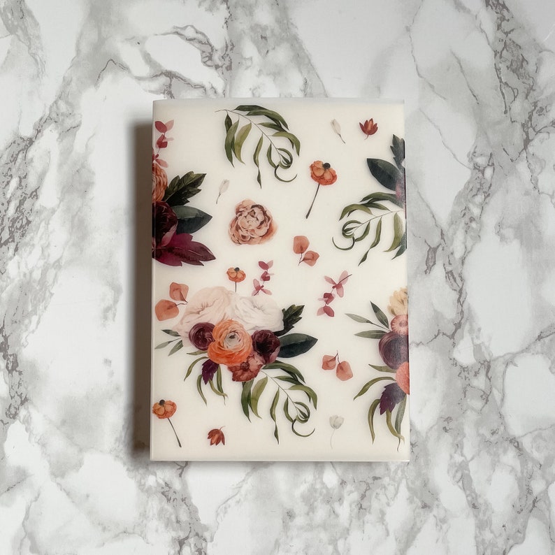 May include: A white sheet of paper with a floral design printed on it. The design features a variety of flowers in shades of pink, red, and orange, with green leaves and stems. The flowers are arranged in a loose, flowing pattern.