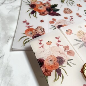 May include: A sheet of clear, translucent paper with a floral design printed on it. The design features a bouquet of pink, orange, and burgundy flowers with green leaves. The flowers are arranged in a loose, flowing style.