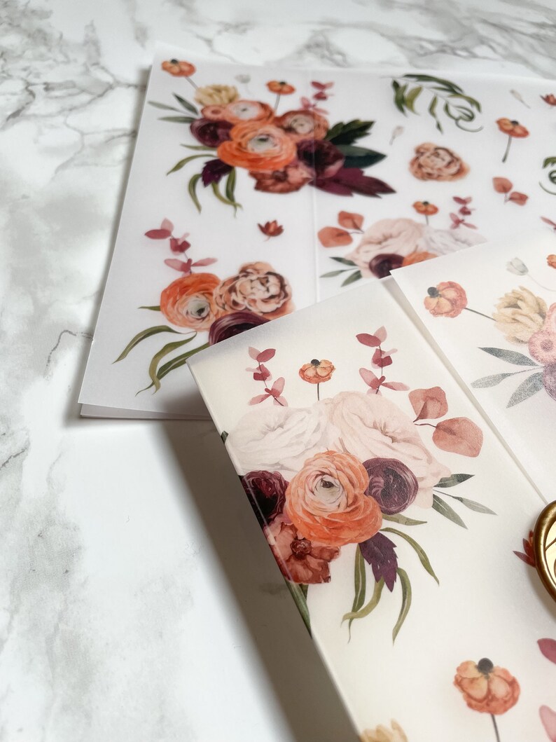 May include: A sheet of clear, translucent paper with a floral design printed on it. The design features a bouquet of pink, orange, and burgundy flowers with green leaves. The flowers are arranged in a loose, flowing style.
