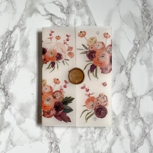 May include: A white envelope with a floral design featuring pink, orange, and burgundy flowers. A gold wax seal with a monogram is in the center of the envelope.