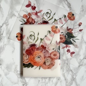 May include: A white card with a floral design featuring pink, red, and orange flowers. The flowers are arranged in a bouquet with green leaves and stems.