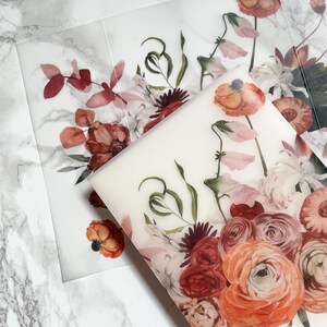 May include: A sheet of clear, translucent paper with a floral design printed on it. The design features a bouquet of red, pink, and orange flowers with green leaves. The flowers are arranged in a loose, natural style.