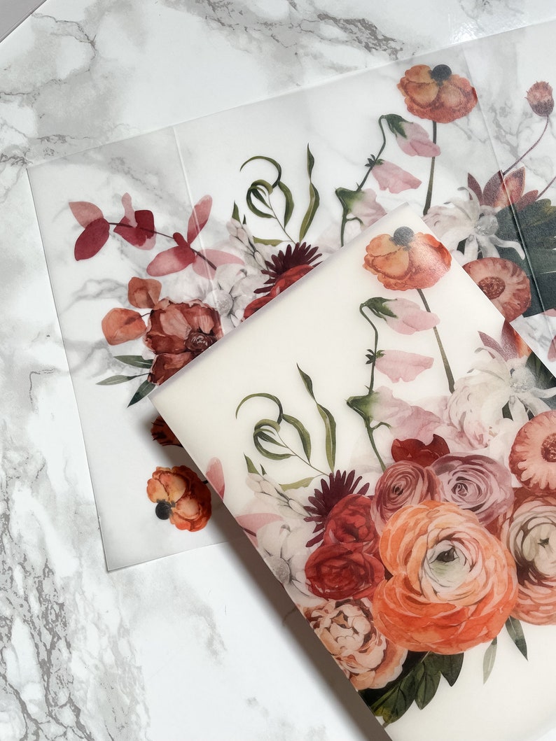 May include: A sheet of clear, translucent paper with a floral design printed on it. The design features a bouquet of red, pink, and orange flowers with green leaves. The flowers are arranged in a loose, natural style.
