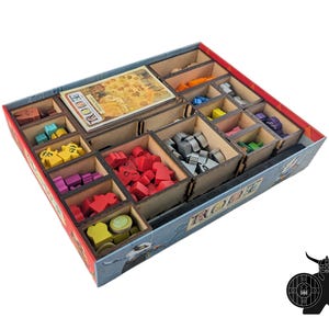 May include: A wooden game organizer with multiple compartments filled with colorful game pieces. The organizer is labeled "ROOT" and features a variety of shapes and colors, including red, yellow, and blue pieces. The box is rectangular with a red border.