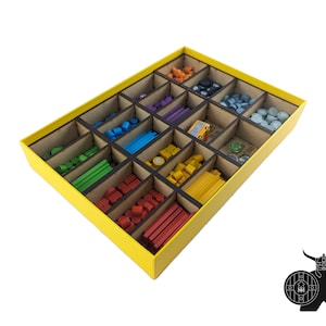 Op de afbeelding: Gele doos met vakken om spelstukken te organiseren. De doos bevat verschillende gekleurde houten stukken, waaronder kubussen, cilinders en kleine schijven.