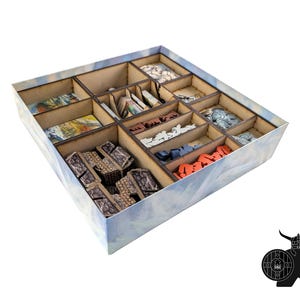 May include: A wooden game organiser with multiple compartments, filled with game pieces in various colours and shapes. The box has a light blue and white exterior with a cloudy design. The organiser is designed to hold board game components.
