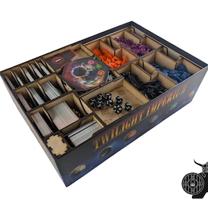 Puede incluir: Un organizador de juegos de madera con múltiples compartimentos para componentes de juegos de mesa. Contiene cartas, dados y varias piezas de juego en naranja, morado y azul. El exterior es negro con la inscripción "TWILIGHT IMPERIAL" en el lateral.