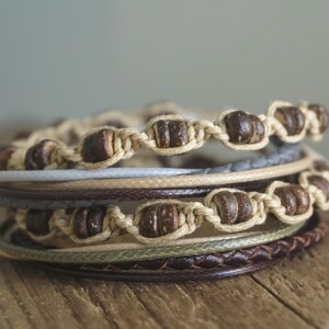 May include: A stack of four bracelets made with brown wooden beads and natural fibers. The bracelets are layered on top of each other, creating a textured and earthy look.