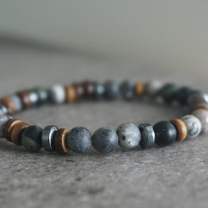 May include: A bracelet made with a variety of beads, including stone, wood, and metal. The bracelet features grey, black, brown, and green beads. This bracelet is suitable for daily wear and offers a natural aesthetic.