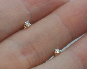 May include: A pair of small, simple diamond stud earrings. The earrings are set in gold and feature a single, round diamond in each earring.