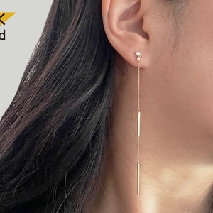 Puede incluir: Pendientes de aro de oro de 14 quilates con una cadena delicada y dos barras pequeñas. Los pendientes tienen un pequeño diamante en la parte superior.