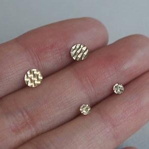 May include: Three gold-toned stud earrings with a textured, geometric design. The earrings are different sizes.