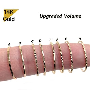 Op de afbeelding: Acht dunne 14K gouden ringen gelabeld van A tot H, elk met een verschillende textuur of gladde afwerking. De ringen zijn in een rij weergegeven en tonen variaties in metaaldetails en lichtreflectie op de gouden banden.