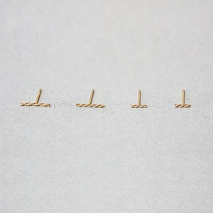 May include: Four gold bar earrings with a twisted design. The earrings are arranged in a row on a light grey surface.