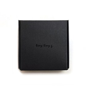Puede incluir: Una caja cuadrada negra con el texto "tiny tiny &" impreso en la parte superior.