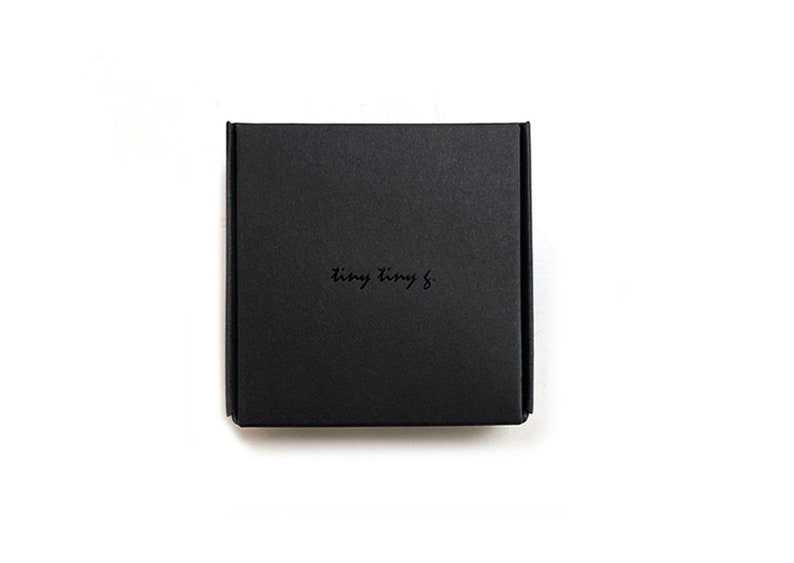 Puede incluir: Una caja cuadrada negra con el texto "tiny tiny &" impreso en la parte superior.