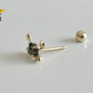 May include: A 14K gold earring featuring a black diamond set in a delicate floral design. The earring is a stud style with a small ball post.