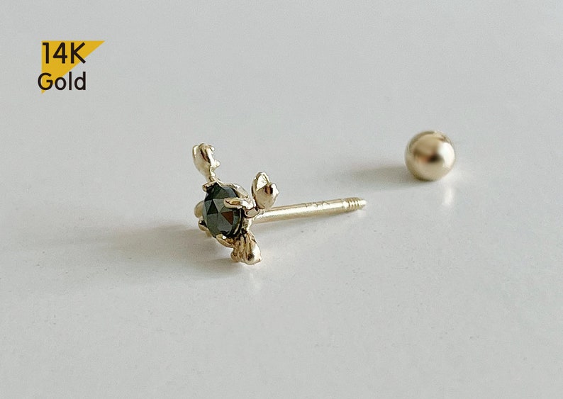 May include: A 14K gold earring featuring a black diamond set in a delicate floral design. The earring is a stud style with a small ball post.