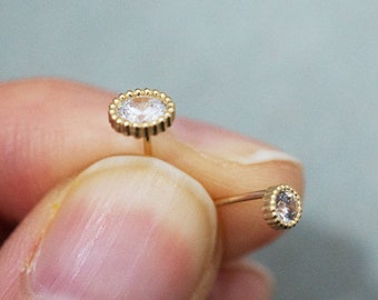 May include: A pair of gold earrings with small, clear gemstones set in a beaded halo.