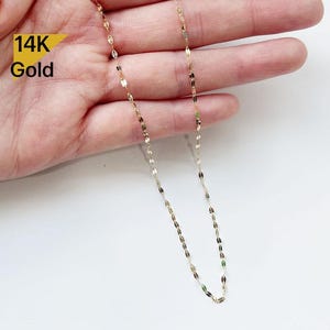 Op de afbeelding: Een 14 karaats gouden ketting met een delicaat, ovaalvormig schakelschema. De ketting wordt getoond op een hand, met de uiteinden van de ketting die naar beneden hangen.