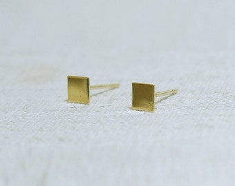 May include: A pair of gold square stud earrings. The earrings are small and simple, with a smooth, polished finish.