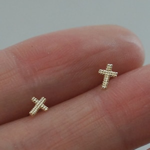 May include: A pair of gold cross earrings. The crosses are small and delicate, with a textured surface.