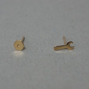 May include: A pair of gold earrings, one shaped like a hexagon and the other shaped like a wrench.